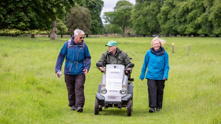 Three ramblers, the middle one on a mobility scooter, come towards the camera